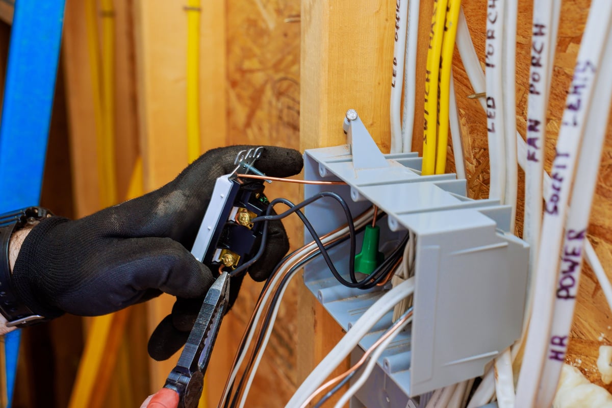 Electrician contractor wearing gloves connects wires to switch light, installation in new home under construction