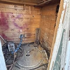 Wooden shed interior with coiled rope, bicycle, and tools stored on brick walls