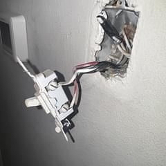 Exposed electrical wall outlet box with white wiring and circuit breaker components visible in drywall opening
